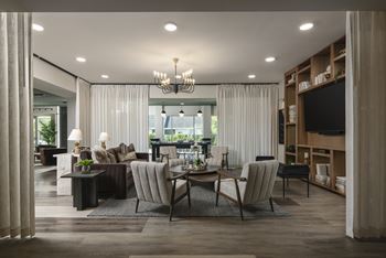 A modern living room with a large window, a sofa, a chair, a coffee table, and a chandelier.